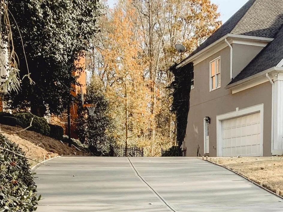 A new concrete driveway with a control joint running up to the garage of a two-story house, form stakes along its edge